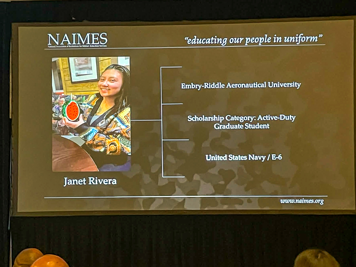 Large projector screen with image of woman in corner and rows of text