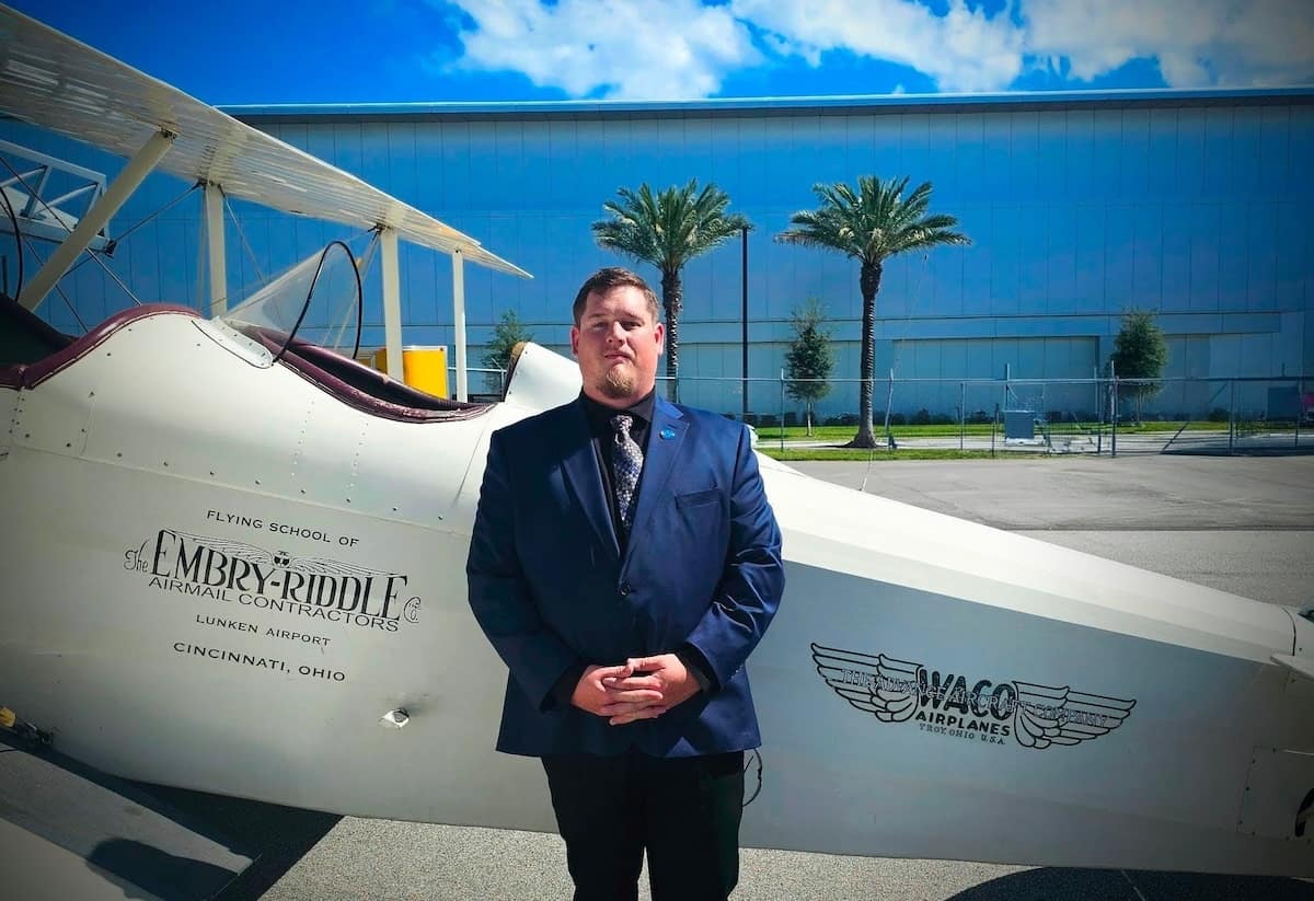 Jacob Pritchard, the first Worldwide Campus student to earn a Research Scholar transcript notation, stands before a vintage Embry-Riddle plane. 