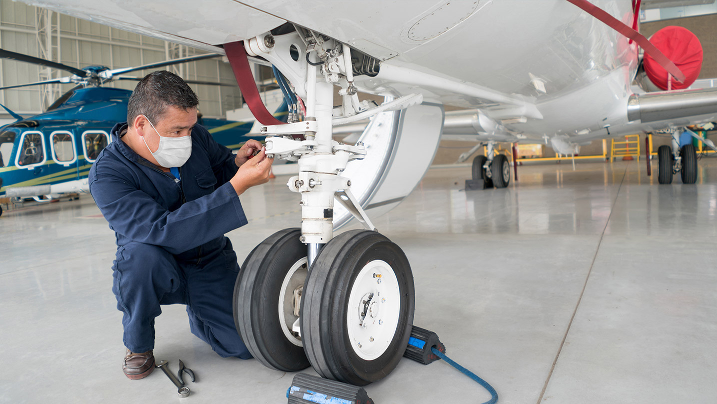 A male aviation technician in a mask working on an airplane.