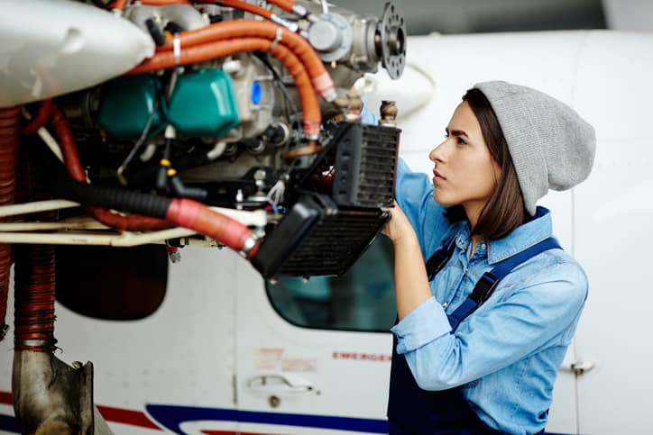 Young woman in uniform fixing an airplane motor