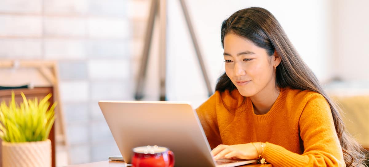 Female student sitting at table, working on laptop