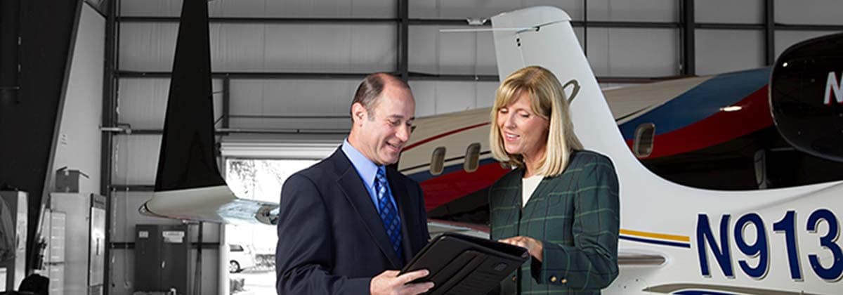 a male and female discuss business in an airplane hangar